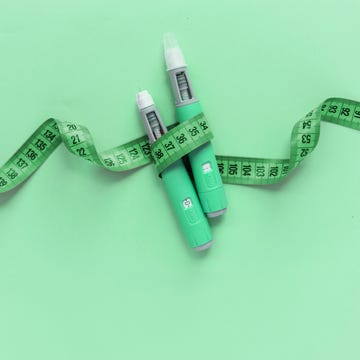 Two injectors dosing pens for subcutaneous injection of antidiabetic medication or anti-obesity medication hovering over a blue background. Yellow measuring tape around the injectors. two injectors dosing pens for subcutaneous injection of antidiabetic medication or anti obesity medication hovering over a blue background yellow measuring tape around the injectors