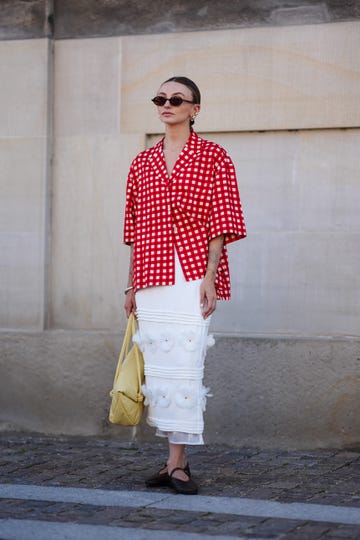 copenhagen, denmark august 6 a guest wears black sunglasses, gold earrings, white and red pattern button up short sleeve shirt, silver bracelet, light yellow leather bag, white midi skirt with floral detail, black flat leather shoes, outside lovechild 1979, during the copenhagen fashion week springsummer 2024 2025 on august 6, 2024 in copenhagen, denmark photo by edward berthelotgetty images