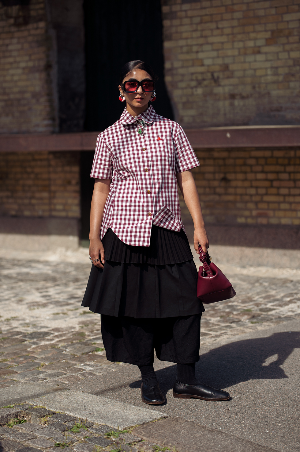 Kopenhagen, Denemarken 7 augustus: een gast draagt ​​een zwarte rok, een wit-rood geruit overhemd, een bordeauxrode tas van Ganni en een oranje zonnebril buiten de Deadwood-show tijdens de derde dag van de Copenhagen Fashion Week (cphfw) SS25 op 7 augustus 2024 in Kopenhagen, Denemarken. (foto door Raimonda Kulikauskiene/Getty Images)