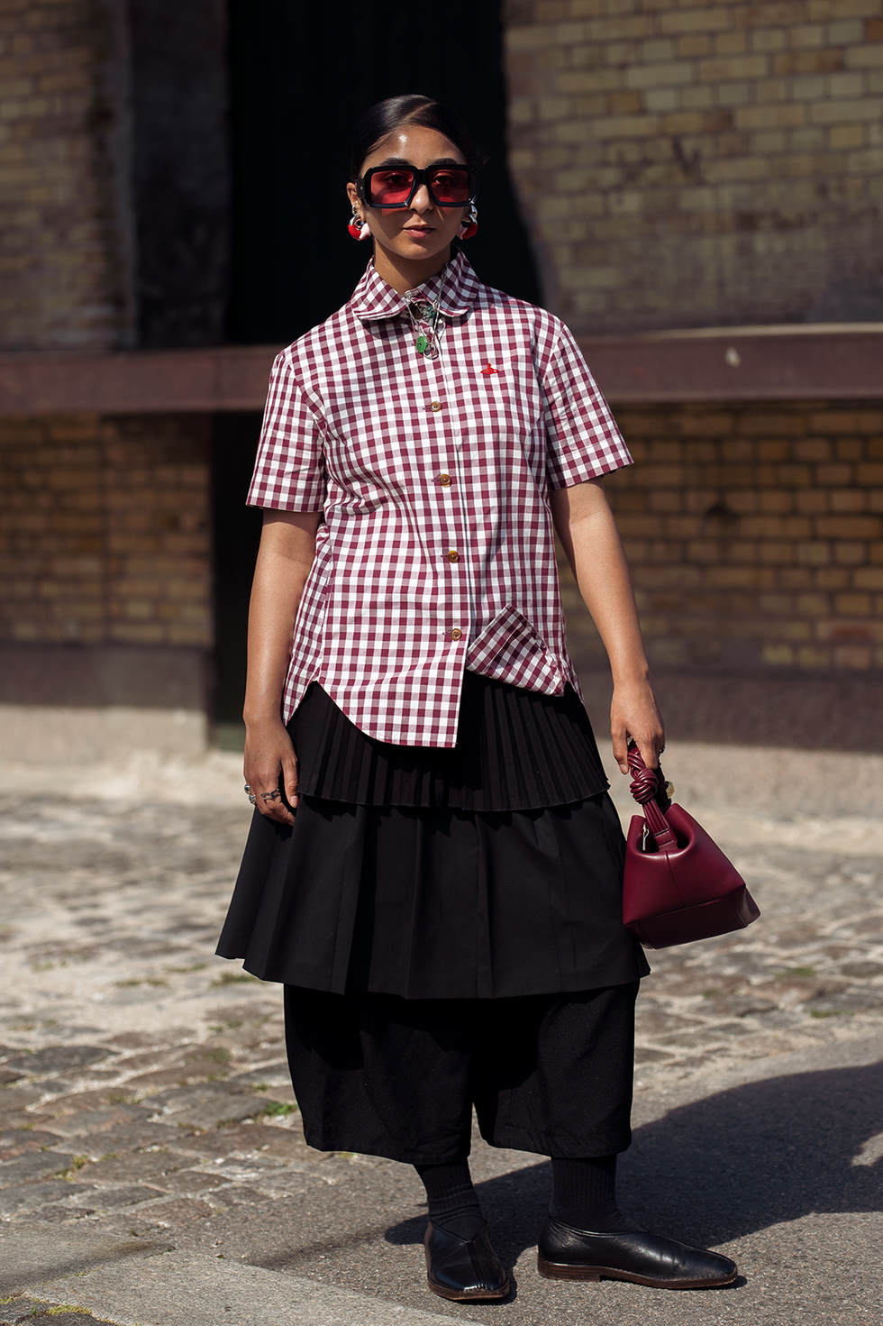 Kopenhagen, Denemarken 7 augustus: een gast draagt een zwarte rok, een wit-rood geruit overhemd, een bordeauxrode tas van Ganni en een oranje zonnebril buiten de Deadwood-show tijdens de derde dag van de Copenhagen Fashion Week (cphfw) SS25 op 7 augustus 2024 in Kopenhagen, Denemarken. (foto door Raimonda Kulikauskiene/Getty Images)