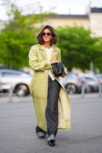 copenhagen, denmark august 7 a guest wears black sunglasses, gold earrings, white shirt, shiny light green leather trench coat, black and white lined pants, shiny black leather bag, outside baum und pferdgarten, during the copenhagen fashion week springsummer 2024 2025 on august 7, 2024 in copenhagen, denmark photo by edward berthelotgetty images