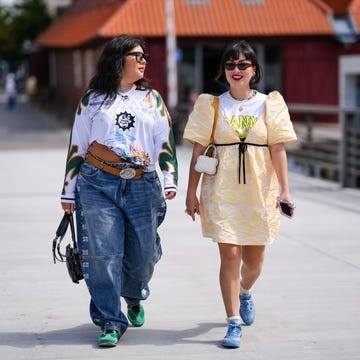 Street Style - Day 4 - Copenhagen Fashion Week SS25 copenhagen, denmark august 8: a guest wears black sunglasses, silver necklace, white graphic print long sleeve shirt, light brown belt, light blue denim jean pants, shiny black leather bag, gold rings, light green sneaker shoes. a guest wears dark brown sunglasses, silver earrings, gold layered necklaces, white t shirt with graphic print, light yellow pattern puffy sleeve mini dress, white bag, light brown bag, silver rings, cream socks, light blue sneakers shoes, outside marimekko, during the copenhagen fashion week spring/summer 2024 2025 on august 8, 2024 in copenhagen, denmark. (photo by edward berthelot/getty images)