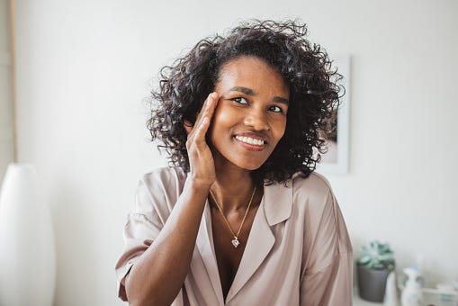 young woman in bathroom applying moisturizing cream on her skin after having a bath