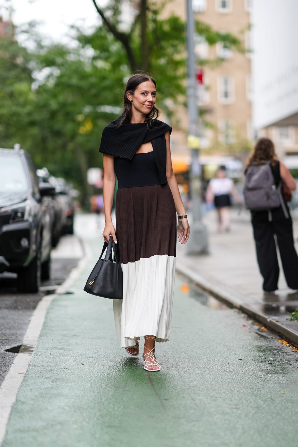 new york, new york september 07 a guest wears black sweater over the shoulders, black tank top, dark brown and white pleated midi skirt, shiny black leather bag, silver bracelet, silver rings, white strappy sandals, outside jonathan cohen, during the new york fashion week springsummer 2025 on september 07, 2024 in new york, new york photo by edward berthelotgetty images