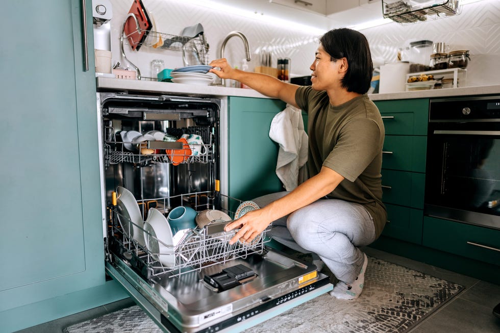 young casually clothed man using dishwasher machine in a domestic kitchen at home