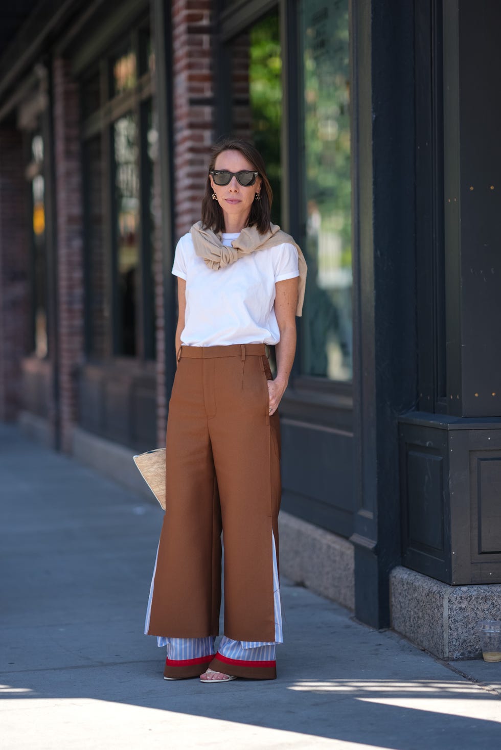 new york, new york september 09 a guest wears black sunglasses, silver earrings, white t shirt, cream beige sweater around shoulders, dark brown layered white and light blue lined undercover pants, white flip flop heels, outside lafayette 148, during the new york fashion week springsummer 2025 on september 9, 2024 in new york, new york photo by edward berthelotgetty images