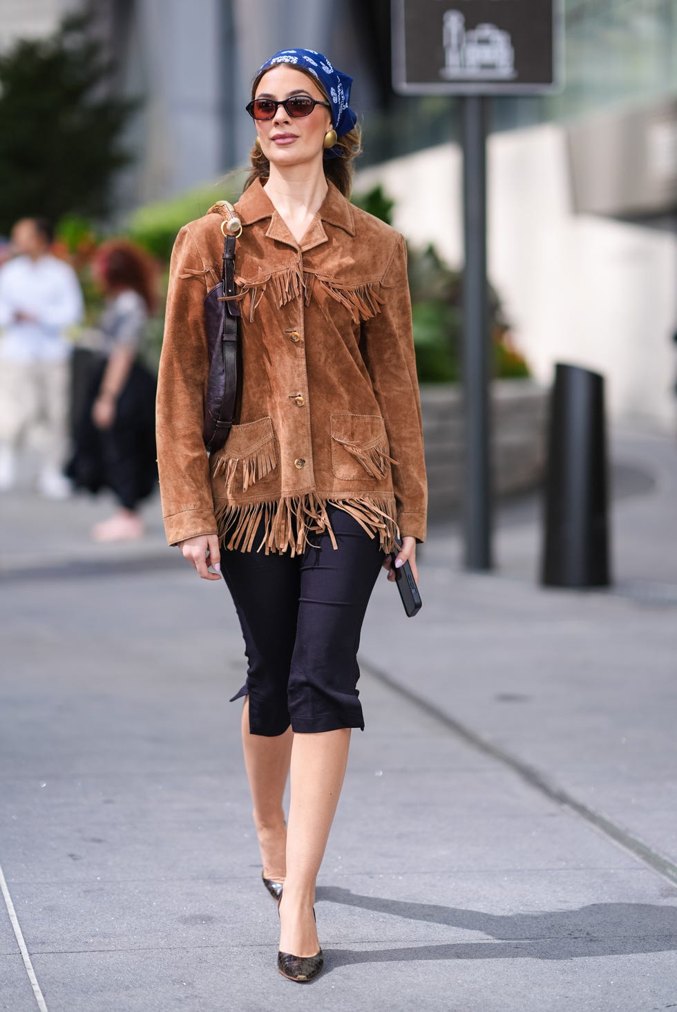 new york, new york september 08 a guest wears dark blue patternprint head scarf, gold earrings, dark brown suede tassel jacket with fringes, black leather bag with gold handle, black capri pants, white pointed toe leather heels, outside jason wu, during the new york fashion week springsummer 2025 on september 08, 2024 in new york, new york photo by edward berthelotgetty images