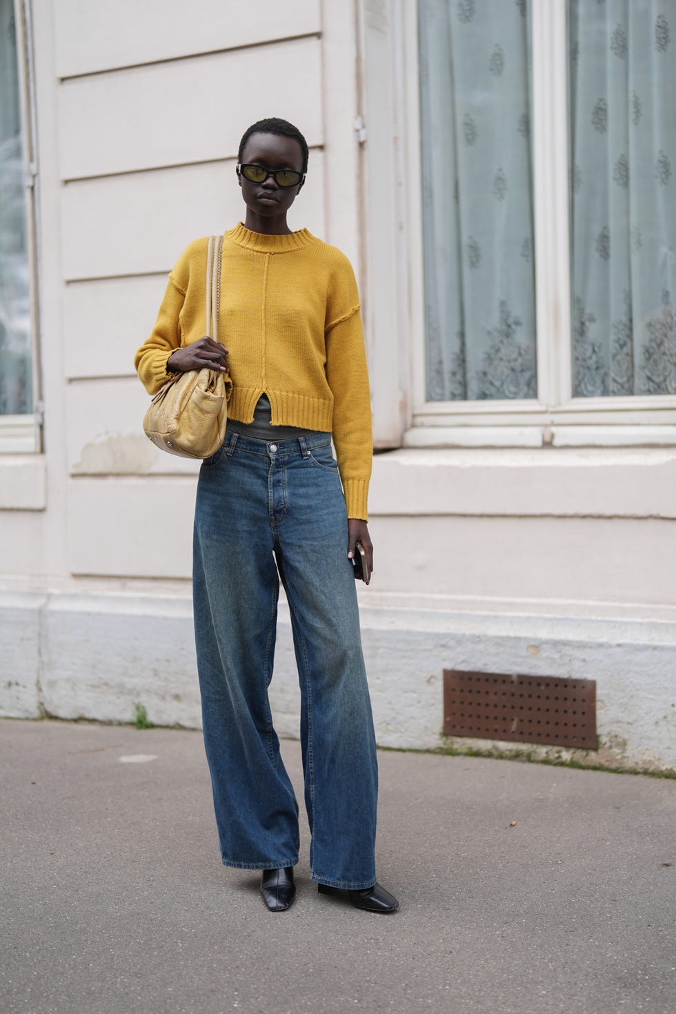 paris, france september 24 a model wears black sunglasses, bright yellow mustard oversized sweater, light yellow leather bag, washed navy blue denim jean pants, shiny black heeled leather boots, outside dior, during the paris fashion week springsummer 2025 on september 24, 2024 in paris, france photo by edward berthelotgetty images