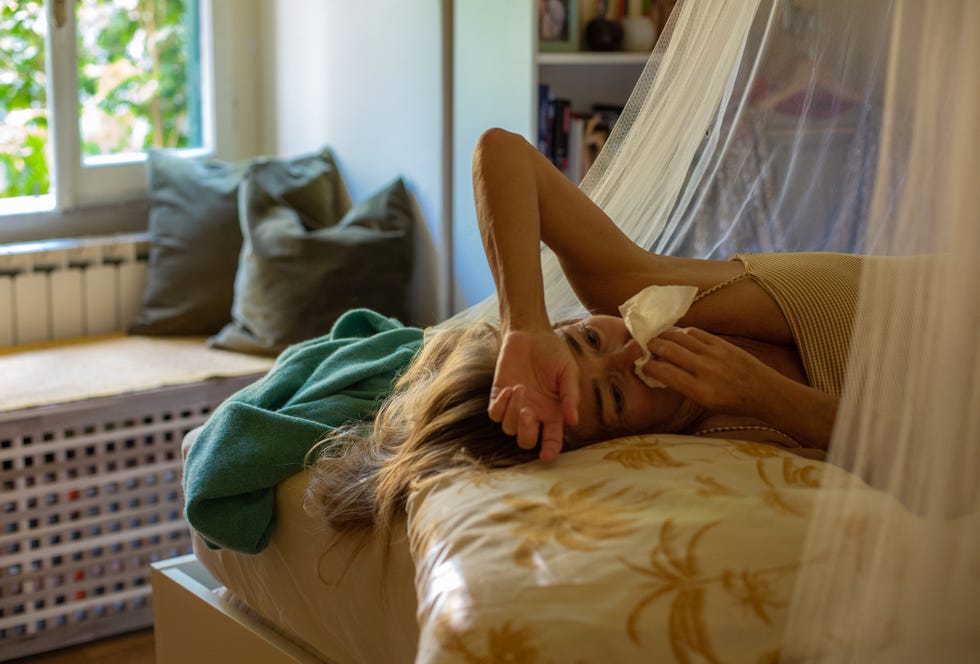 woman lying in bed with a cold, blowing her nose
