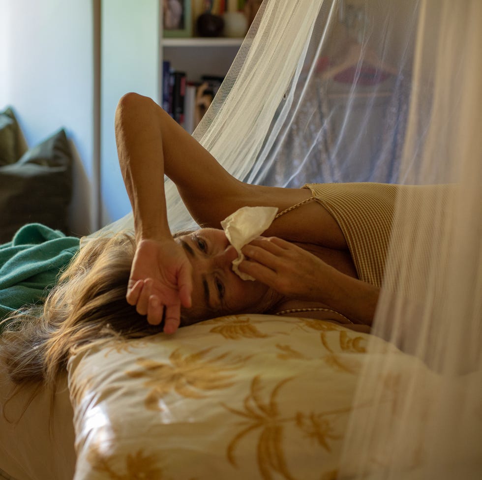 Woman lying in bed with a cold, blowing her nose woman lying in bed with a cold, blowing her nose
