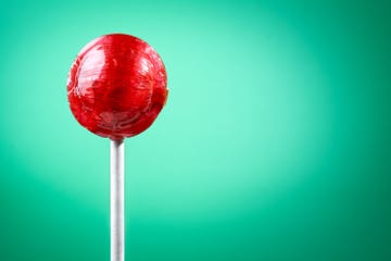 red lollipop on a white stick against a green background