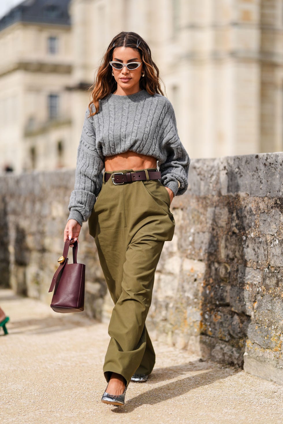 paris, france september 27 camila coelho wears silver sunglasses, silver earrings, dark gray knit cropped sweater, dark brown leather belt, dark green olive baggy loewe pants, dark red leather bag, shiny silver detail loewe heels leather shoes, outside loewe, during the paris fashion week springsummer 2025 on september 27, 2024 in paris, france photo by edward berthelotgetty images