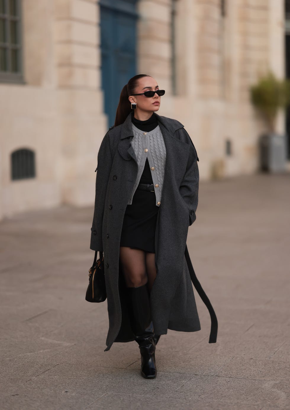 paris, france september 28 anna wein is seen wearing narrow black oval sunglasses from saint laurent chunky squared earrings in gold with a black stone a grey buttoned knit cardigan, paired with a black turtleneck underneath a black mini skirt a black leather belt with a gold buckle an oversized ankle length anthracite wool trench coat featuring a double button placket, sleeve and shoulder tabs, a long belt, and a lapel collar from black palms a rectangular black leather bag with gold details and bag charms from miu miu black tights and knee high shiny black leather boots with a squared toe from hm studio during paris fashion week on september 28, 2024 in paris, france photo by jeremy moellergetty images