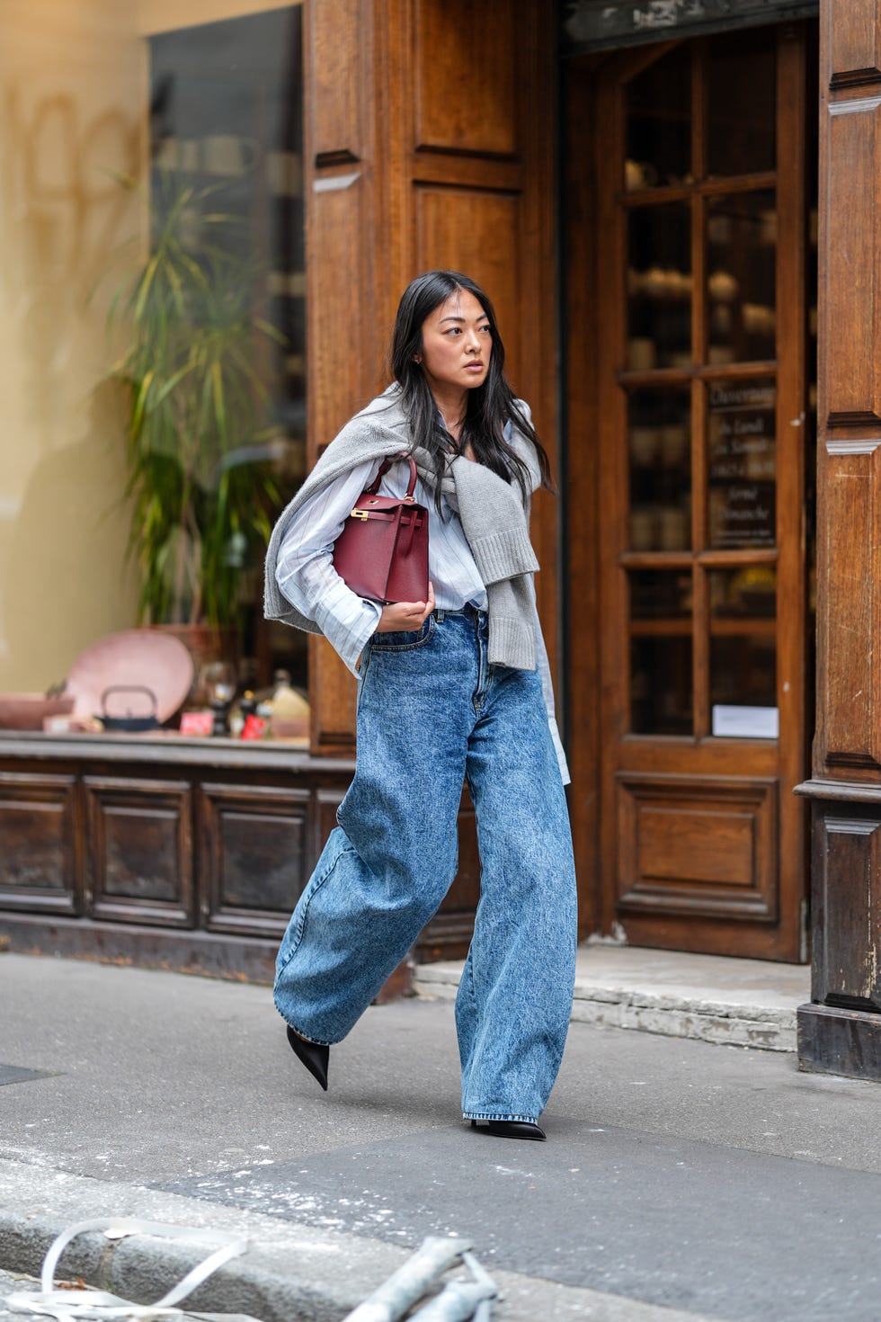 paris, france september 30 a guest wears white linen buttoned up long sleeve shirt, light gray sweater wrapped around shoulders, dark red hermes birkin leather bag, acid washed denim jean loose pants, black pointed toe heels, outside sacai, during the paris fashion week springsummer 2025 on september 30, 2024 in paris, france photo by edward berthelotgetty images