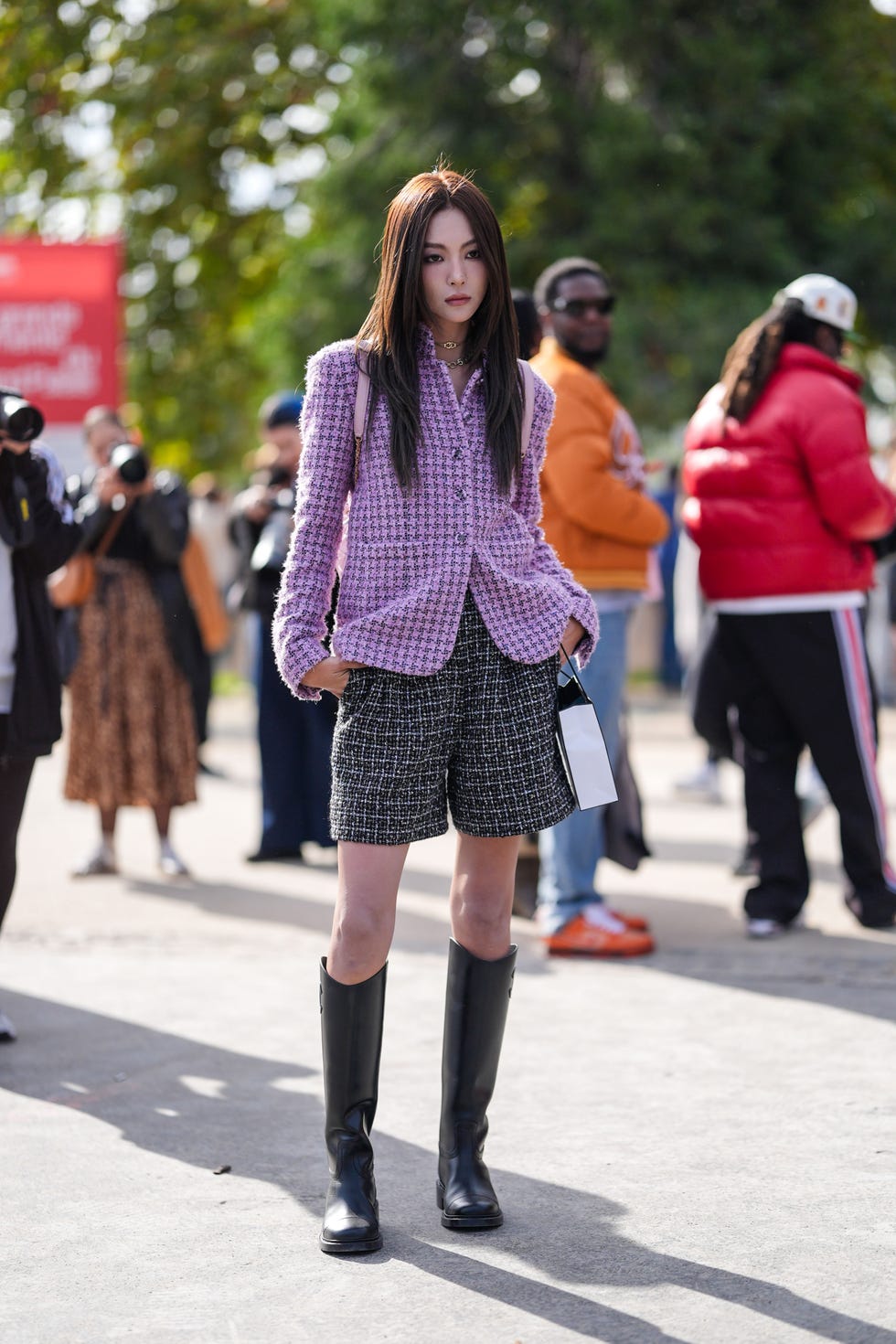 a person stands confidently, dressed in a pink textured blazer over a white top and black shorts