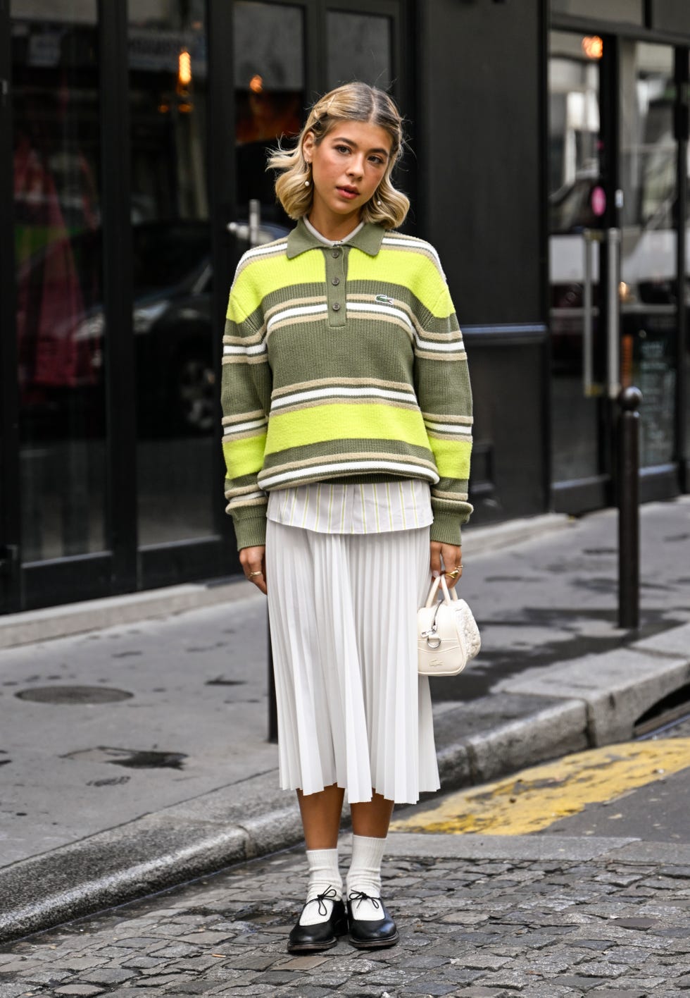 paris, france october 01 ines isaias is seen wearing a green striped lacoste sweater, white shirt, white panel skirt, white socks, black shoes and lacoste white bag outside the lacoste show during womenswear springsummer 2025 as part of paris fashion week on october 01, 2024 in paris, france photo by daniel zuchnikgetty images