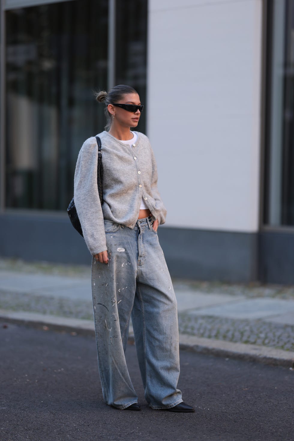 berlin, germany october 12 sophia geiss is seen wearing rectangular black sunglasses with a wide tapered temple from prada, two different sized gold hoop earrings, a silver nose ring, a partly buttoned grey wool cardigan with round neckline from american vintage, a cropped white top underneath, light blue wide legged jeans with baggy fit and black and white paint and smudge details from acne studios, a silver ring, a black leather woven shoulder bag from abro, and pointed black leather boots from leger on october 12, 2024 in berlin, germany photo by jeremy moellergetty images