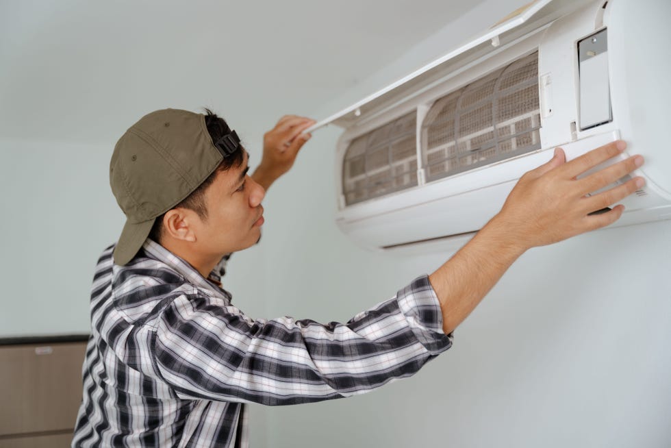 close up of a young asian man inspecting the filter of his air conditioner at home, focused and diligent, modern interior, white walls and sleek design.