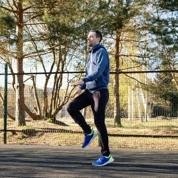 Man performing high-knee warm-up exercises in sunny outdoor park man in a blue hoodie and sportswear practices high knee exercises on a clear day in a public park. his active lifestyle is highlighted by the vibrant outdoor setting and focused energy.