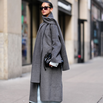 a person wearing a grey coat with a scarf and holding a black handbag