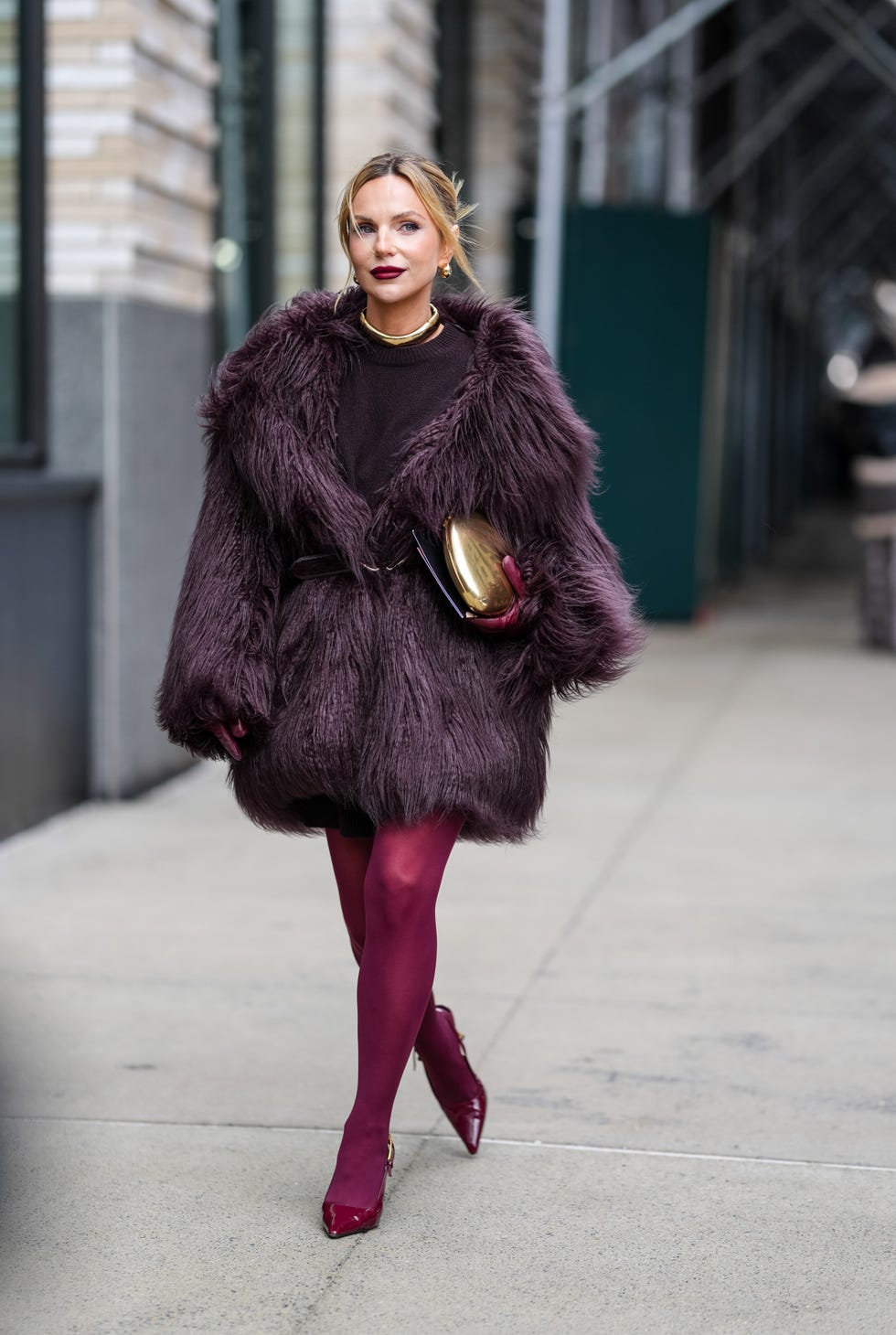 new york, new york february 09 a guest wears gold earrings, gold necklace, burgundy bordeaux sweater, burgundy bordeaux faux fur coat, shiny black leather belt, shiny gold clutch, burgundy bordeaux tights, burgundy bordeaux pointed toe heels leather shoes, outside ulla johnson, during the new york fashion week fallwinter 2025 on february 9, 2025 in new york, new york photo by edward berthelotgetty images