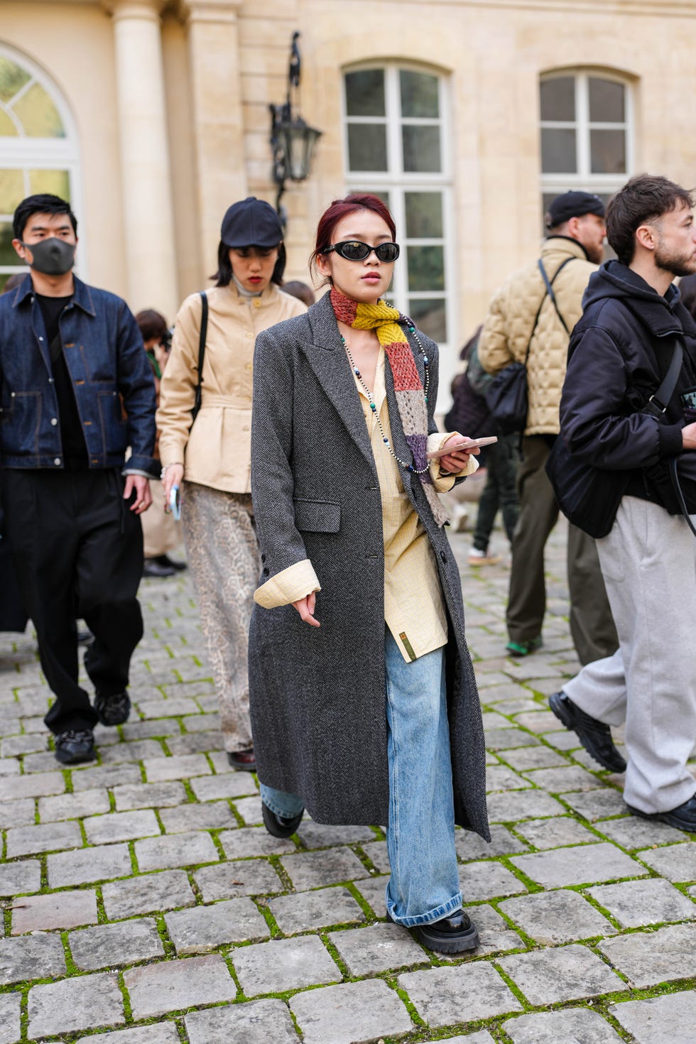 paris, france march 04: a guest wears black sunglasses, dark yellow dark red gray dark purple knit scarf, light pale yellow lined buttoned up oversized t shirt, dark gray wool coat, light blue washed denim jean pants, shiny black boots leather shoes, outside ganni, during the paris fashion week womens fall/winter 2025 2026 on march 4, 2025 in paris, france. (photo by edward berthelot/getty images)