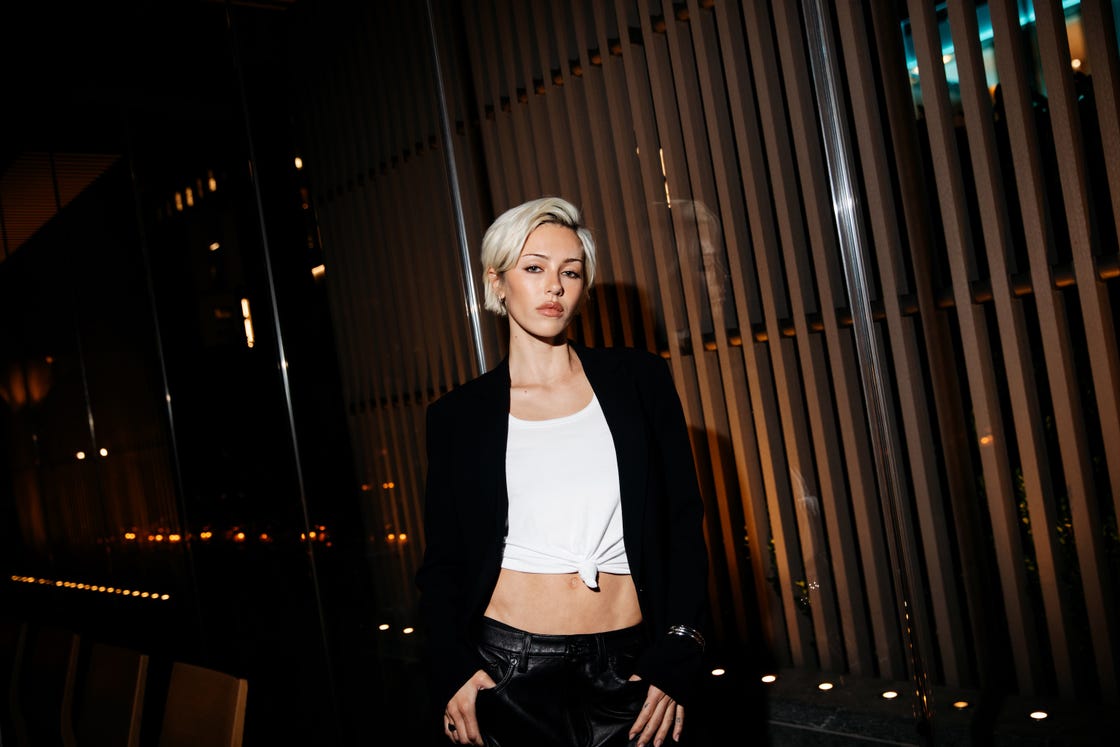 a person wearing a cropped white top and a black blazer against a modern illuminated backdrop