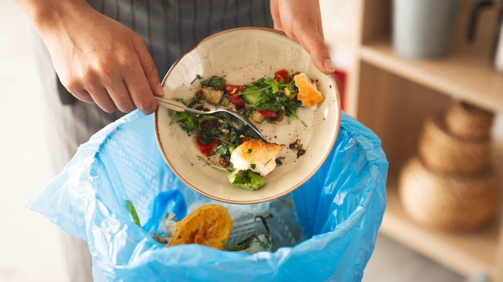 woman scraping leftover food from plate into trash bin in kitchen