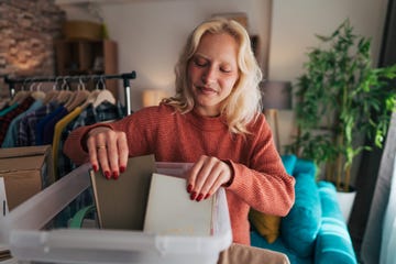 young woman organizing clothes and books while sorting them into plastic boxes during spring cleaning in her living room, creating a tidy and inviting space