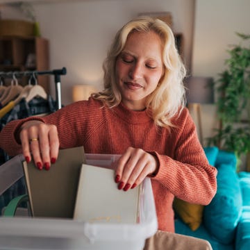 easy-decluttering-hacks young woman organizing clothes and books while sorting them into plastic boxes during spring cleaning in her living room, creating a tidy and inviting space