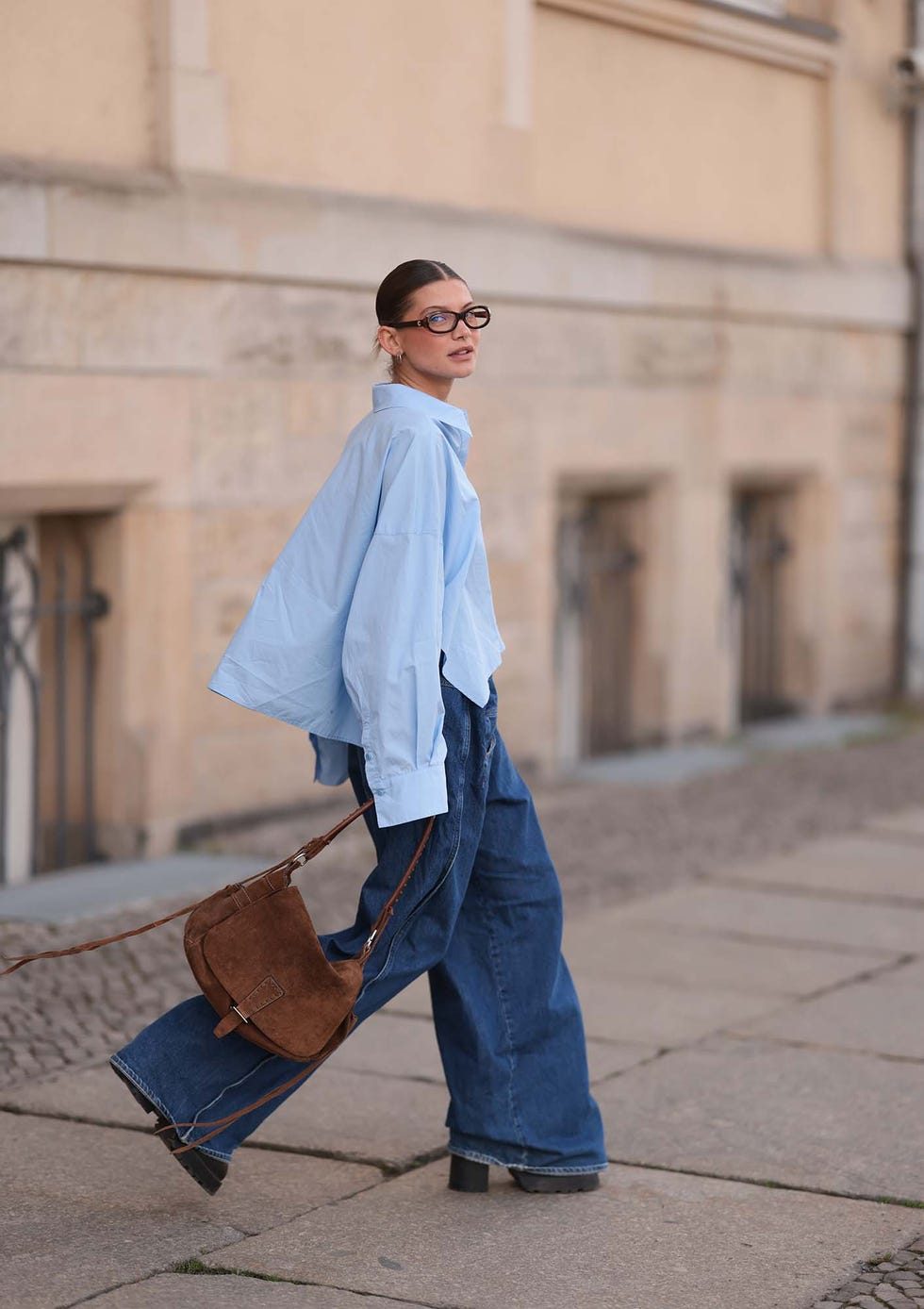 berlin, germany april 22: sophia geiss is seen wearing two different sized silver hoop earrings, oval brown glasses from corlin, a silver nose ring, an oversized light blue shirt from drykorn, wide leg jeans with orange decorative seams from closed, a brown vintage suede bag, and dark brown leather boots with chunky soles from miista on april 22, 2025 in berlin, germany. (photo by jeremy moeller/getty images)