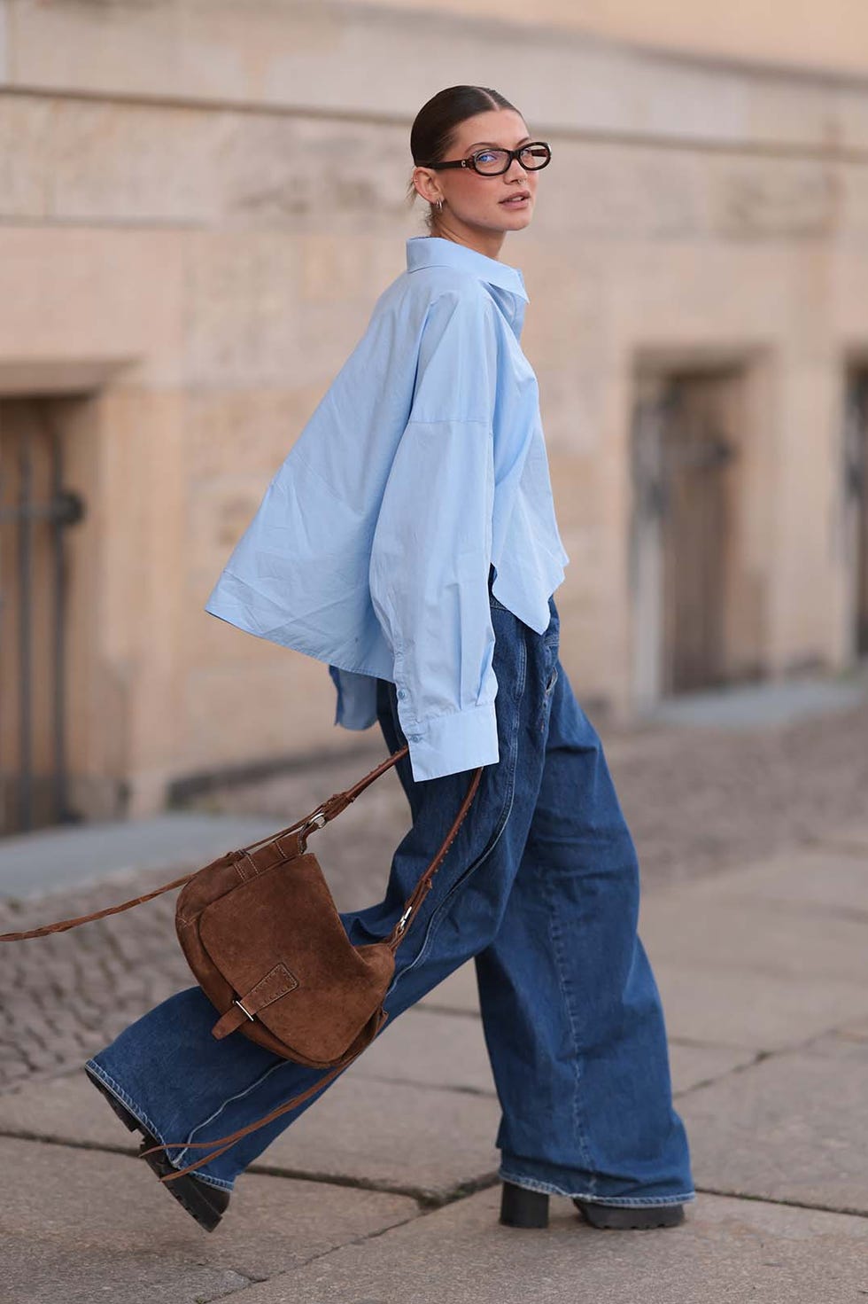 berlin, germany april 22: sophia geiss is seen wearing two different sized silver hoop earrings, oval brown glasses from corlin, a silver nose ring, an oversized light blue shirt from drykorn, wide leg jeans with orange decorative seams from closed, a brown vintage suede bag, and dark brown leather boots with chunky soles from miista on april 22, 2025 in berlin, germany. (photo by jeremy moeller/getty images)