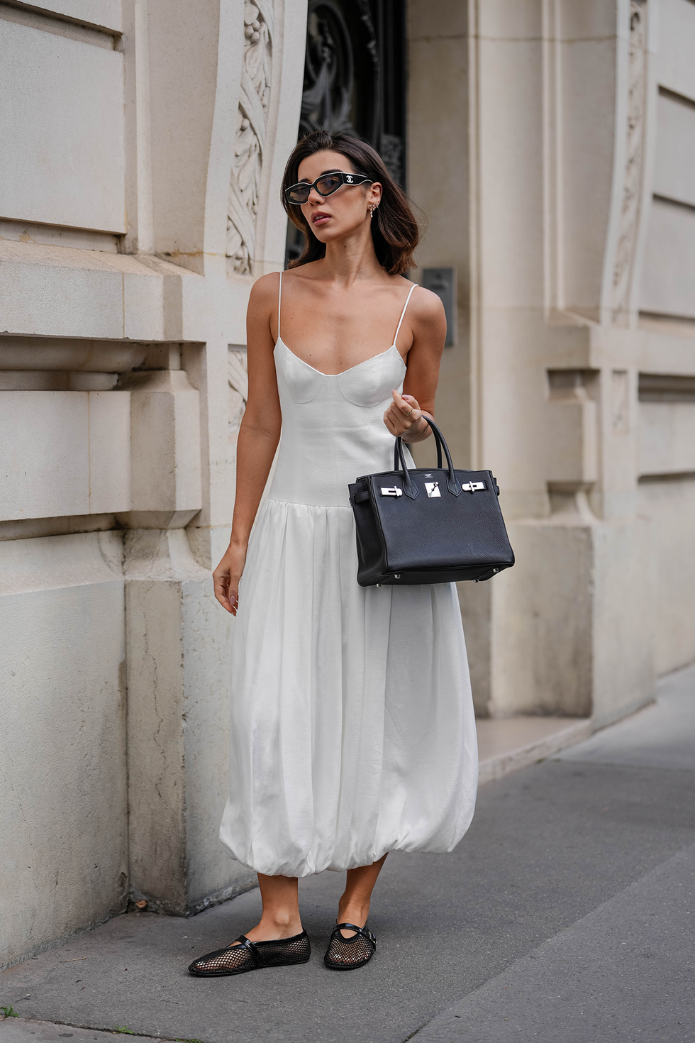 paris, france may 07: katie degas @katie.one wears a white bustier style bubble midi dress with thin spaghetti straps and a voluminous balloon hem by shona joy. black cat eye dual tone sunglasses by chanel are worn with shoulder length straight brown hair styled with a side part. a black textured leather birkin handbag by hermes is carried in the left hand. black fishnet ballet flats by alaia complete the look. full body shot, during a street style fashion photo session, on may 07, 2025 in paris, france. (photo by edward berthelot/getty images)