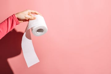young woman holding toilet paper roll on pink background.