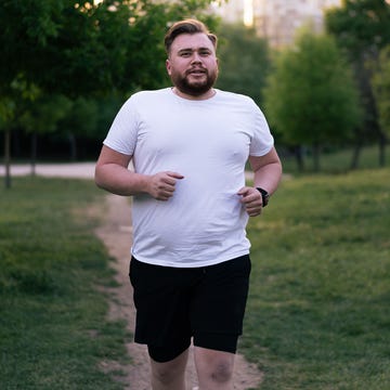Young overweight man running in a city park for weight loss determined overweight man jogging in a park, embracing a healthy lifestyle through exercise and physical activity