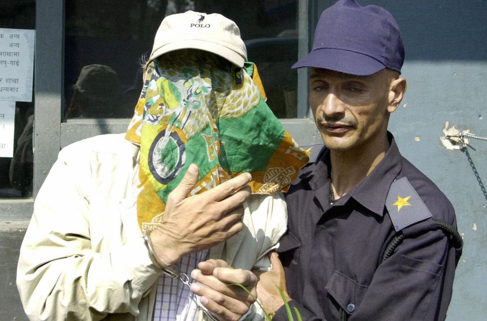 kathmandu, nepal  a nepalese policeman r escorts convicted criminal and french national charles sobhraj l his face covered by a handkerchief at the entrance to kathmandu district court, kathmandu, 16 october 2003   sobhraj, who has been accused of more than 20 murders of young westerners across asia, was arrested in kathmandu on 19 september, for allegedly entering nepal in 1975 with a dutch passport issued in the name of bentinja henricus but with a changed photograph  afp photodevendra m singh  photo credit should read devendra m singhafp via getty images