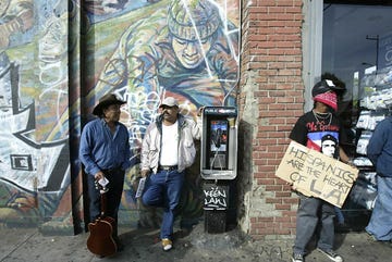 a demonstrator holds a sign as bystanders chat during a rally against california governor arnold schwarzenegger in east los angeles 12 december, 2003 the demonstration was called by a group immigrant rights associations and immigrant advocates asking latinos for an economic strike in the state of california to protest the proposed repeal of a law signed by former governor gray davis