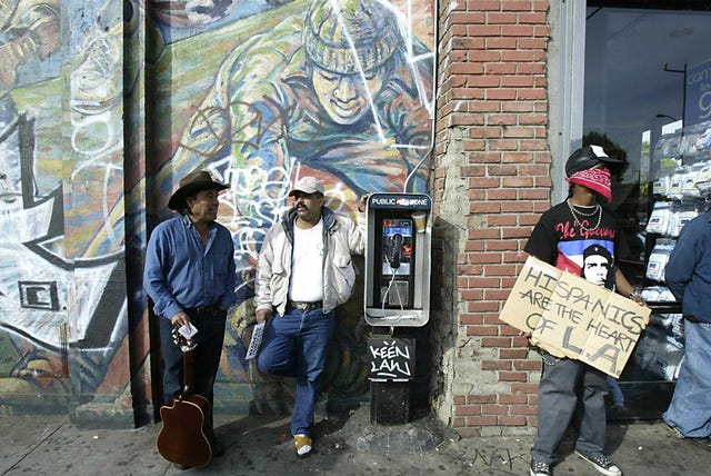 a demonstrator holds a sign as bystanders chat during a rally against california governor arnold schwarzenegger in east los angeles 12 december, 2003 the demonstration was called by a group immigrant rights associations and immigrant advocates asking latinos for an economic strike in the state of california to protest the proposed repeal of a law signed by former governor gray davis