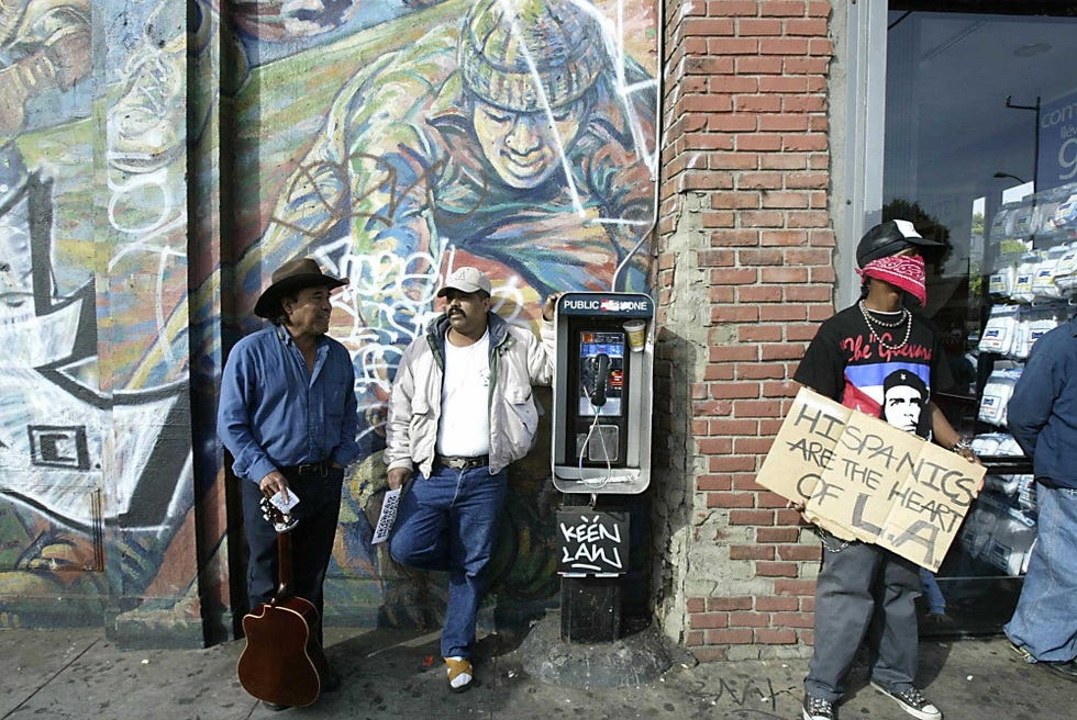 a demonstrator holds a sign as bystanders chat during a rally against california governor arnold schwarzenegger in east los angeles 12 december, 2003 the demonstration was called by a group immigrant rights associations and immigrant advocates asking latinos for an economic strike in the state of california to protest the proposed repeal of a law signed by former governor gray davis