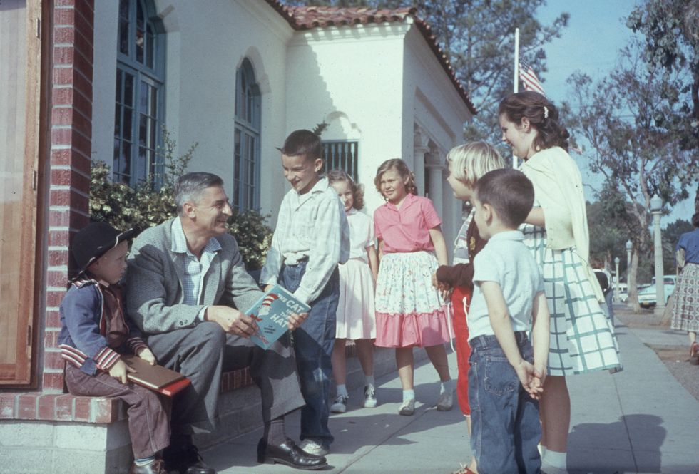 dr seuss talking with a group of children while holding a copy of the cat in the hat in la jolla california, on april 25 1957