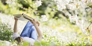 Woman reading book in grass under tree with white blossoms