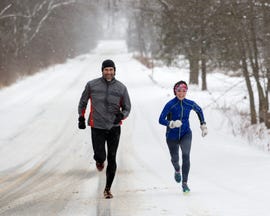 male and female running sprinting up a snowy hill during a winter training run