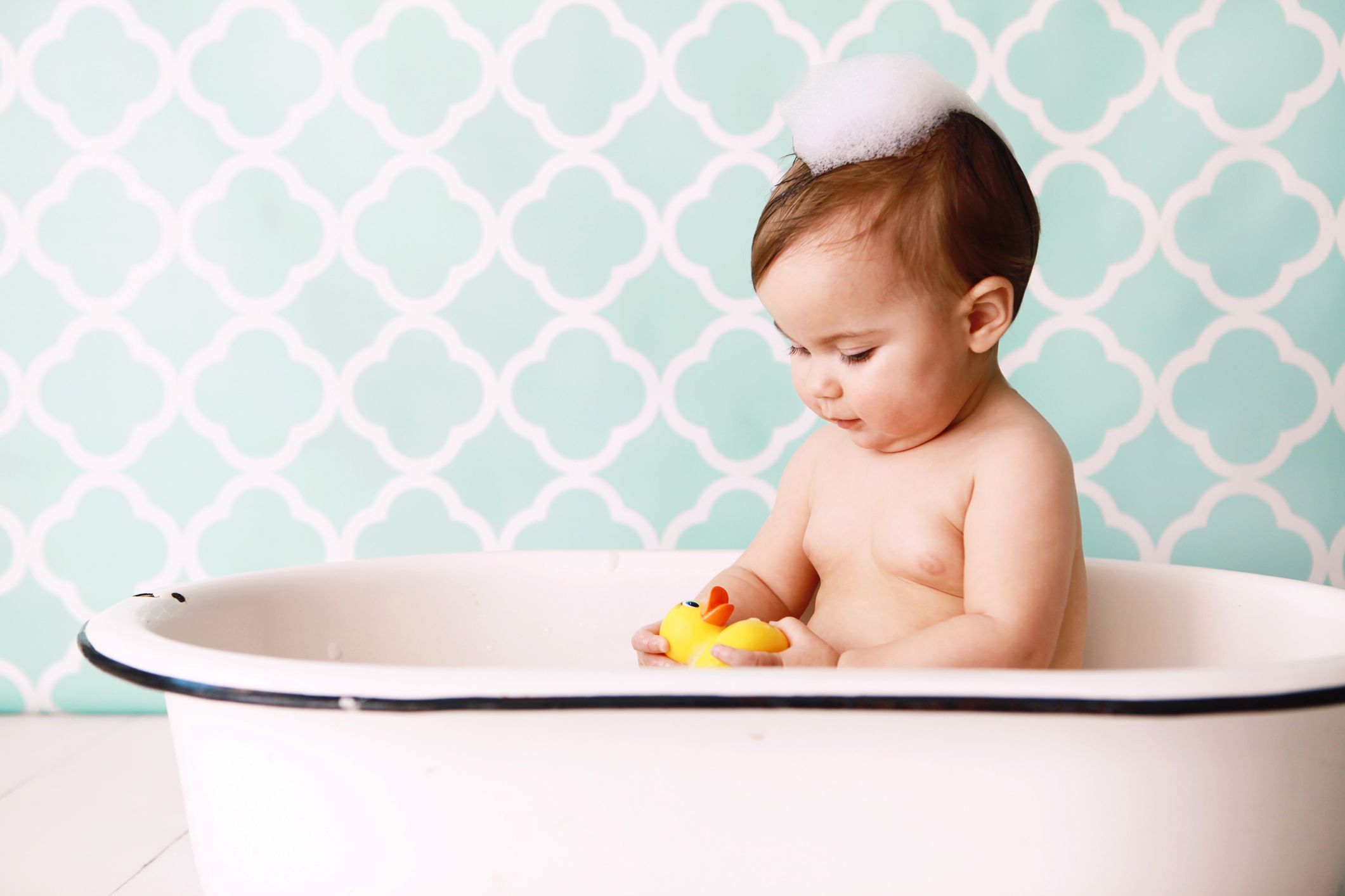 a baby looks at a rubber ducky as she sits in an antique bathtub copy space in vintage wallpaper