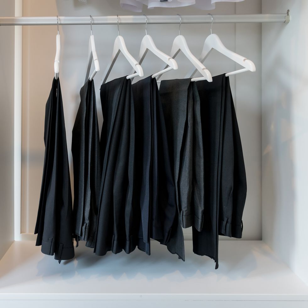 row of pants hanging on coat hanger in white wardrobe