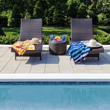 two pool chairs with beach towels and straw hats and a table with two glasses and a tray of fruit by a pool