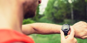 runner on mountain forest trail checking looking at sportwatch smart watch, cross country runner checking performance, gps position or heart rate pulse sport smartwatch and fitness equipment in use outdoors in nature on summer trail