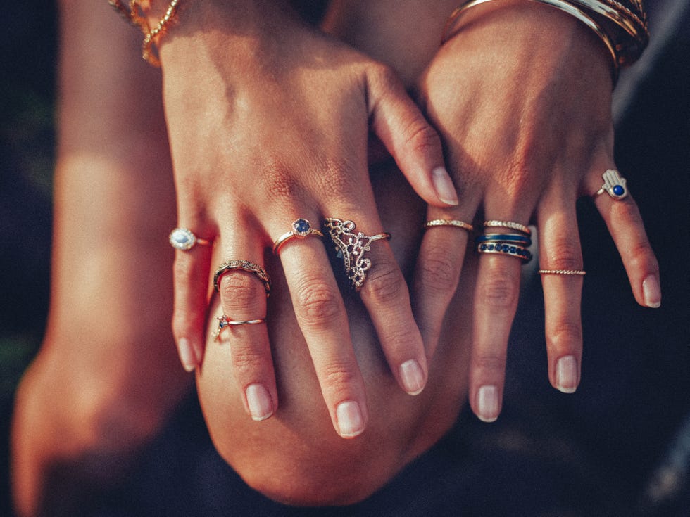 cropped closeup of a boho girls hands with many rings on her fingers, in gold and silver with dark blue stones
