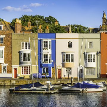 colourful cottages and narrow higgledy piggledy homes reflecting in the tranquil harbour of a quaint fishing port under the blue summer skies of weymouth, dorset, uk prophoto rgb profile for maximum color fidelity and gamut