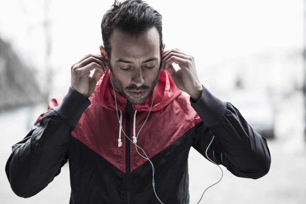 Sporty man in jacket adjusting headphones