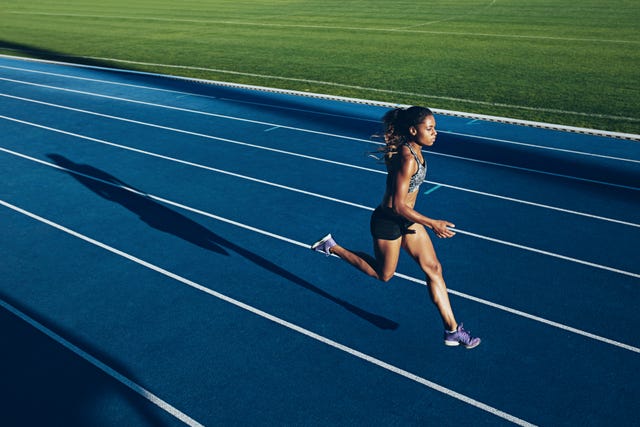 outdoor shot of young african woman athlete running on racetrack. professional sportswoman during running training session.